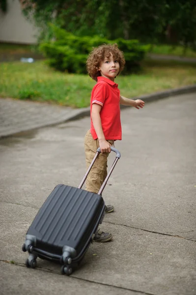 The boy of 8-9 years drags a big suitcase on castors.