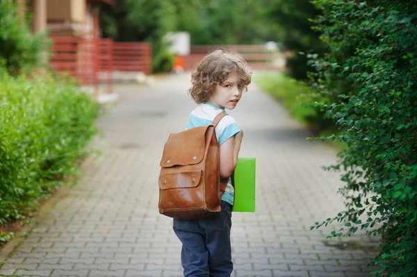 Schoolboy goes to school with a satchel behind shoulders.