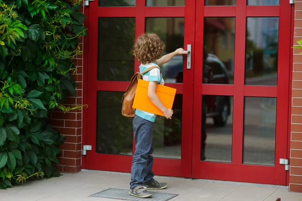 The little first grader opens a door of school.