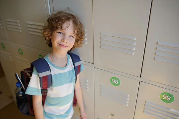 Little schoolboy standing near lockers in school hallway.