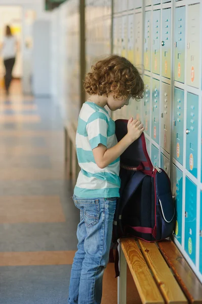 Little schoolboy standing near lockers in school hallway.