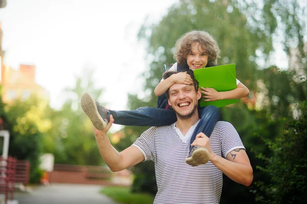 Little schoolboy sitting on the shoulders of father and clings to his head