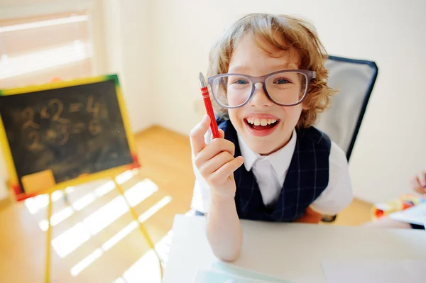 Funny little student bespectacled sits at school desk.