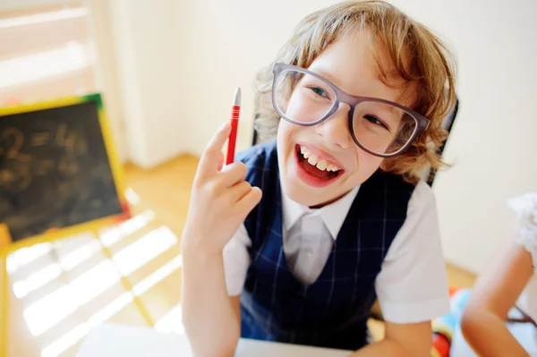 Funny little student bespectacled sits at school desk.