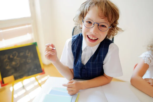 Funny little schoolboy in glasses sits at a school desk.