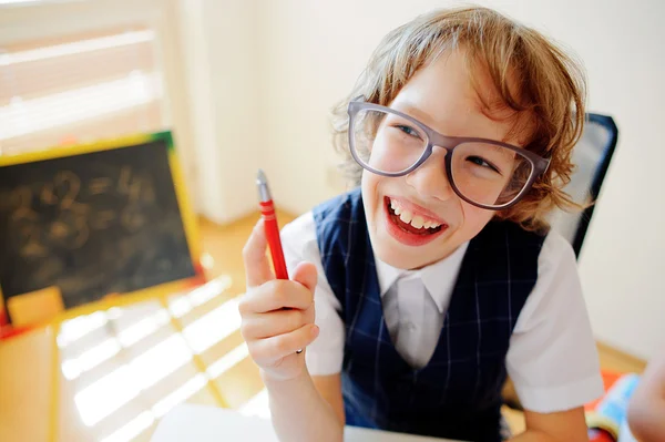 Funny little schoolboy in glasses sits at a school desk.
