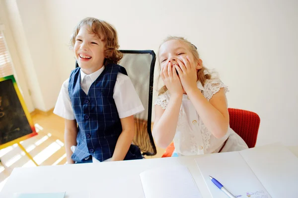 Funny little schoolchildren, boy and girl, sit at one desk.