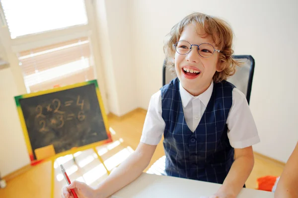 Cheerful little student bespectacled sits at school desk.