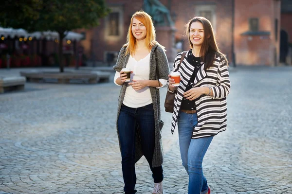 Two cute girlfriends go on an empty morning streets of old European city.