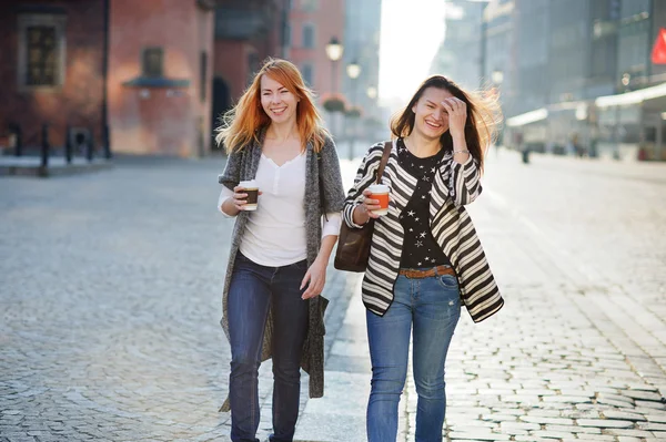 Two cute girlfriends go on an empty morning streets of old European city.