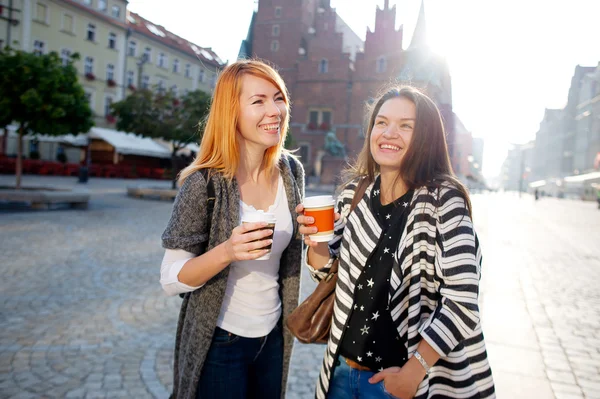 Two young women are happy to drink coffee in the center of the beautiful European city.