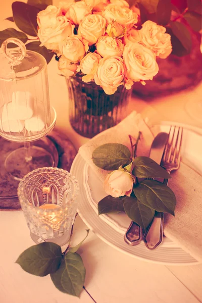 Vintage wedding table decorations with roses, candles, cutlery a