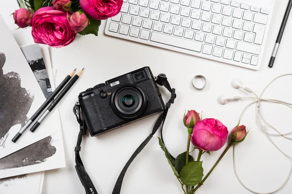 Modern computer keyboard, pink flowers and photo camera on white