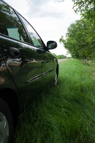 Black car on the side of the road in the green grass