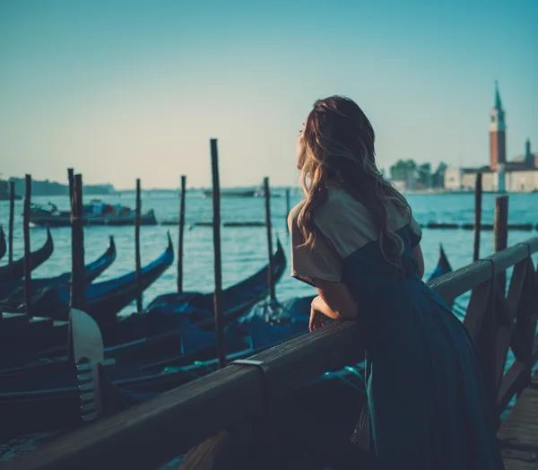 Beautiful well-dressed woman standing near San Marco square with gondolas and Santa Lucia island on the background.