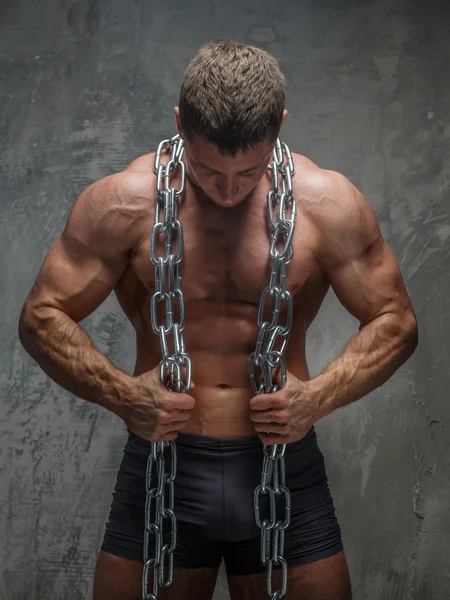 Big bodybuilder showing his body and holding steel chain