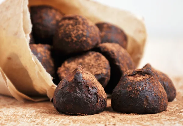 Chocolate truffles with cocoa powder in a paper packing on the wooden table, closeup