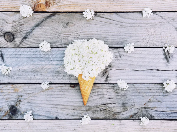 White hydrangea flowers in ice cream cone on rustic wooden background. Stylish flat lay. Minimal concept. Summer pattern.