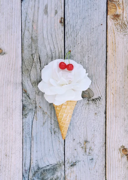 White rose flower topped with a red cherries in ice cream cone on rustic wooden background. Stylish flat lay. Minimal concept. Vanilla ice cream.