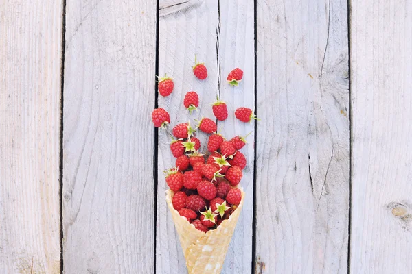 Ripe fresh raspberries in ice cream cone on rustic wooden background. Stylish flat lay. Minimal concept.