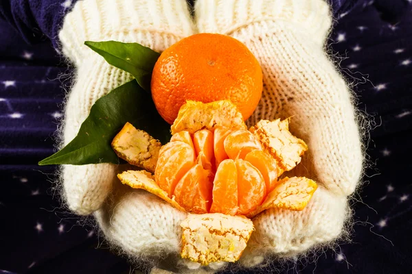 Hands in knitted white mittens holding tangerines