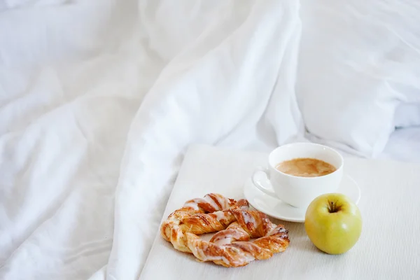 Tray with breakfast on a bed. Sweet pretzel, Cup of coffee and Apple