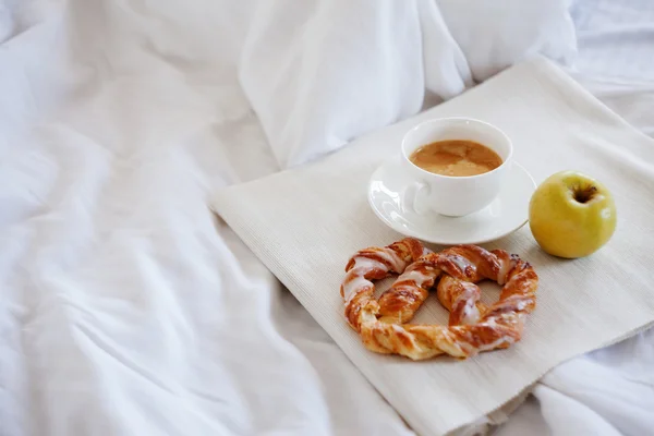 Tray with breakfast on a bed. Sweet pretzel, Cup of coffee and Apple