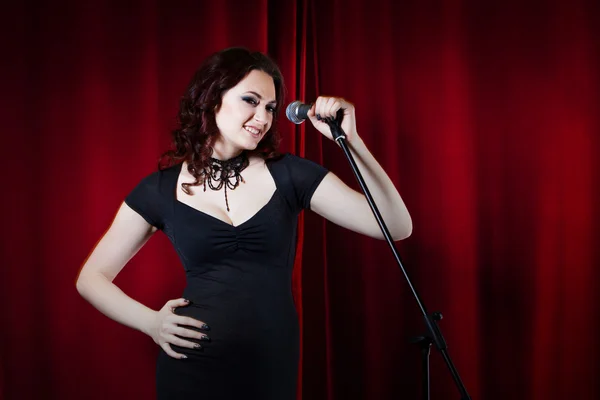 Beautiful Singing Girl on stage. Beauty Woman with Microphone. Red curtain  background