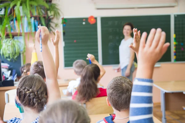 Children at desks with hands raised