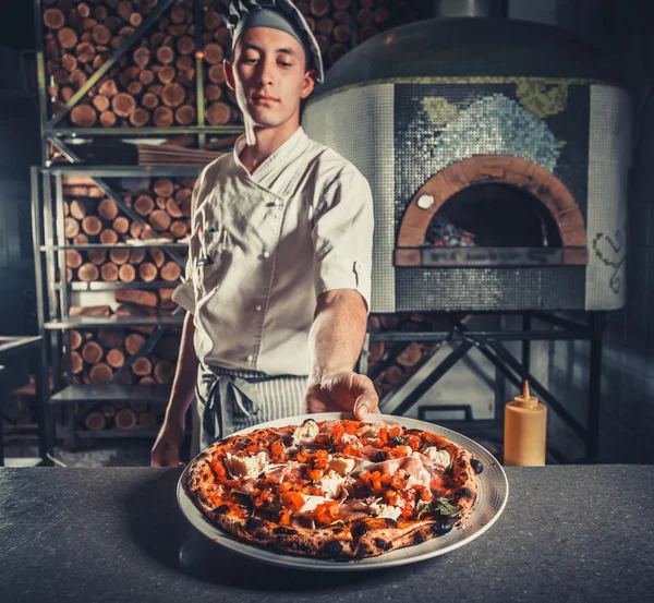 Male cook holding fresh cooked pizza