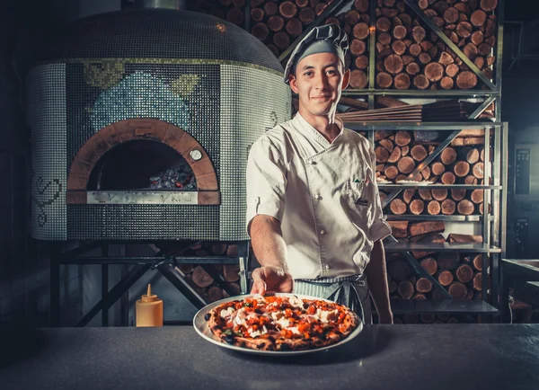 Male cook holding fresh cooked pizza