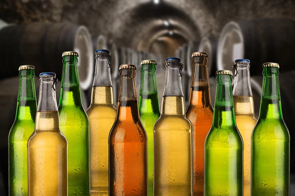 Group of cold wet beer bottles in the cellar with vintage kegs