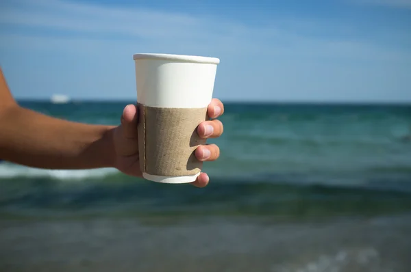 Paper cup with coffee in hand on the sea background