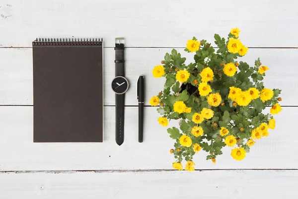 Notepad, wrist watch, pen and flower vase on a wooden table