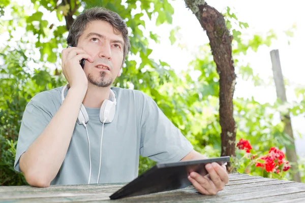 Young man at the phone and tablet pc with headphones, outdoor
