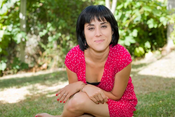 Young casual woman posing seated, smiling at the camera, outdoors