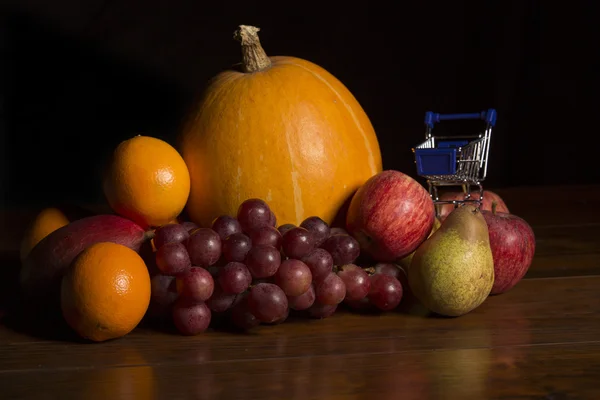 Variety of fruits and a small shopping cart on a woden table, studio picture