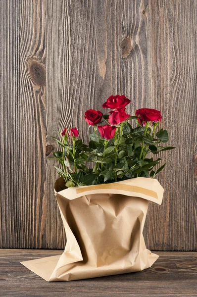 Red rose flowers in paper-bag on a wooden background