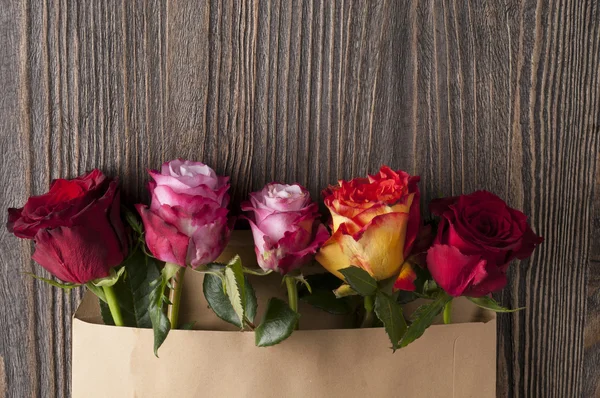 Bunch of multicolor rose flowers in paper envelope over wooden b