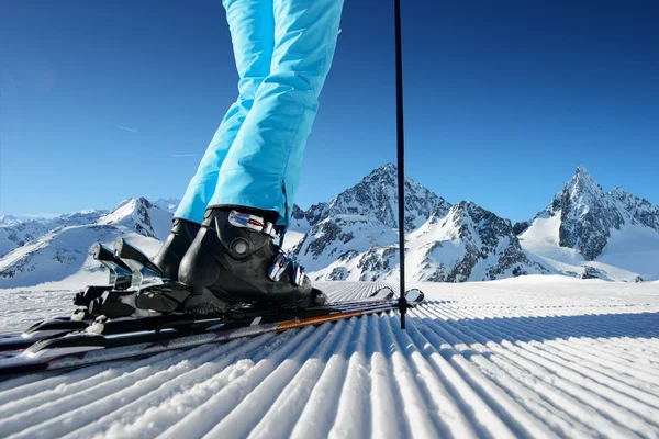 Girl on ski standing on the fresh snow on newly groomed ski piste at sunny day in mountains