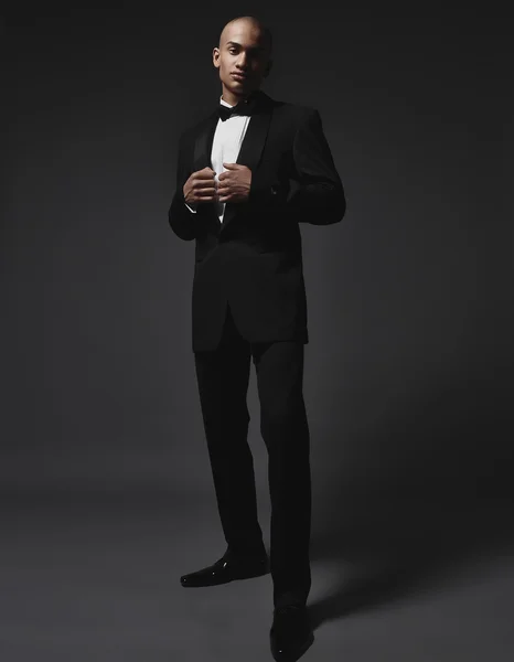 Studio fashion portrait of a handsome young African American businessman wearing a black suit and tie
