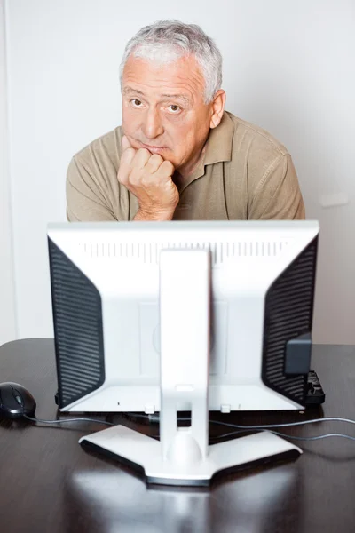 Serious Senior Man Sitting At Computer Desk In Class