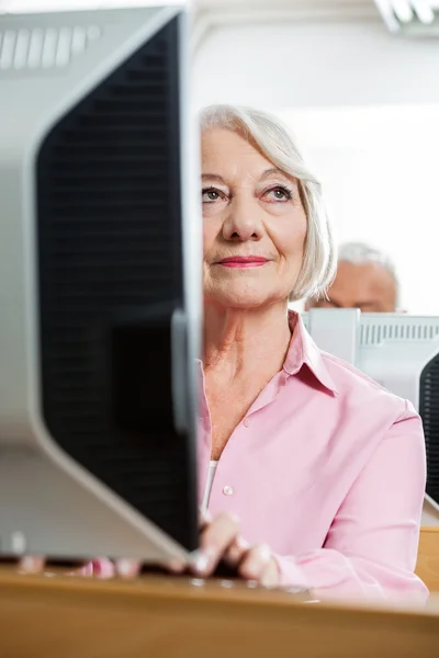 Thoughtful Senior Woman Using Computer In Classroom