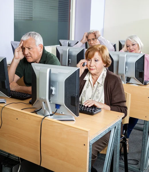 Tensed Senior Students Looking At Computers In Classroom