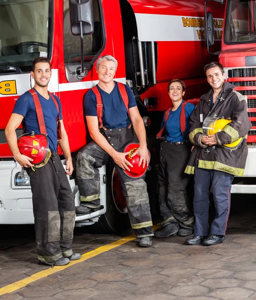 Portrait Of Smiling Firefighters Leaning On Trucks