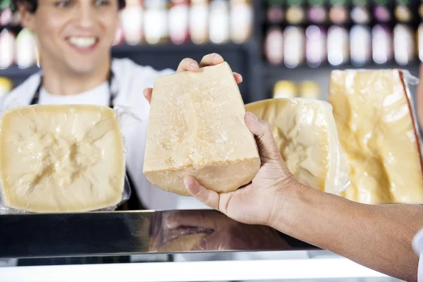 Salesmans Hand Passing Cheese To Colleague In Shop