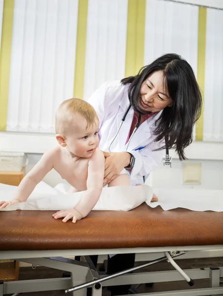 Pediatrician Looking At Baby Crawling On Bed