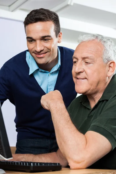 Smiling Teacher Using Computer With Senior Student