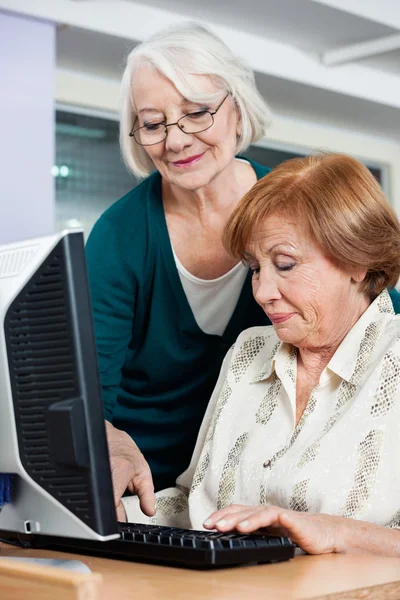 Woman Assisting Female Friend In Using Computer At Classroom