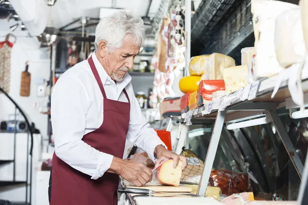 Salesman Slicing Cheese In Shop